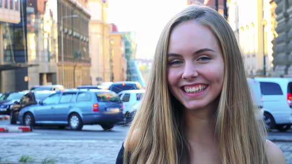 Young Beautiful Woman Smiles To Camera in the City - Street in the Background