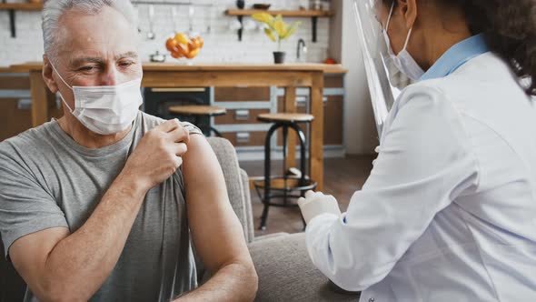 Female Doctor in Protective Mask and Face Shield Injecting Vaccine Into Shoulder of an Elderly