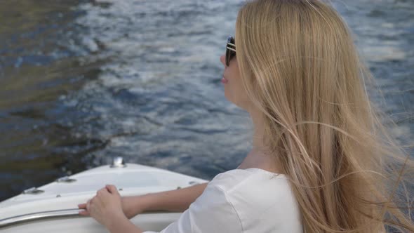 Blonde Young Woman in Sunglasses Sails in Boat on Dark Water