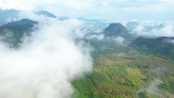 4K Aerial view from a drone flying above rural clouds, road in a tropical forest in Thailand