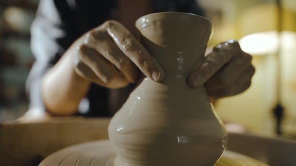 Young Female Potter Gently Pulls the Neck of a Clay Vessel on a Potter's Wheel