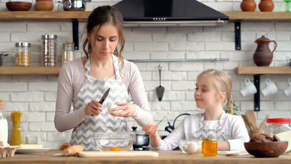 Mother and cute little daughter cooking together at the kitchen.
