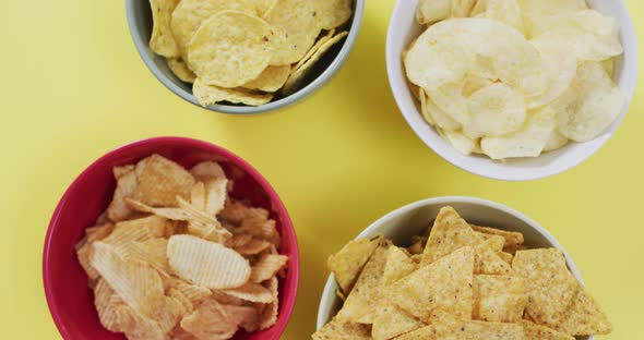 Close up of four bowls full of variety of chips with copy space on yellow surface