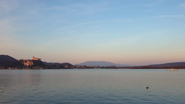 Ferryboat sails on Maggiore Lake at sunset with Angera fortress in background. Static shot