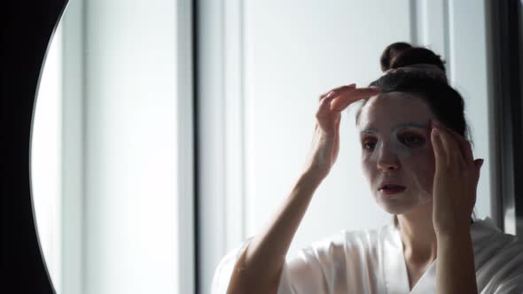 Woman in the Bathroom in Front of the Mirror Puts on a Rejuvenating Face Mask From Wrinkles