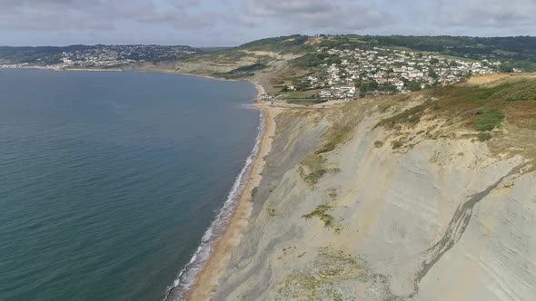 Aerial tracking above the Jurassic coast toward the village of Charmouth, Dorset. Cliffs, sea and th