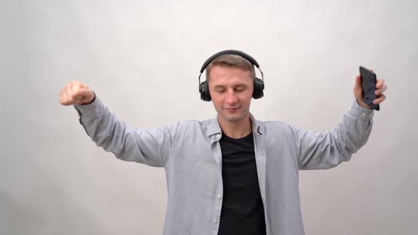 Young Man on a White Background in Headphones and a Smartphone Listens To Music and Dances