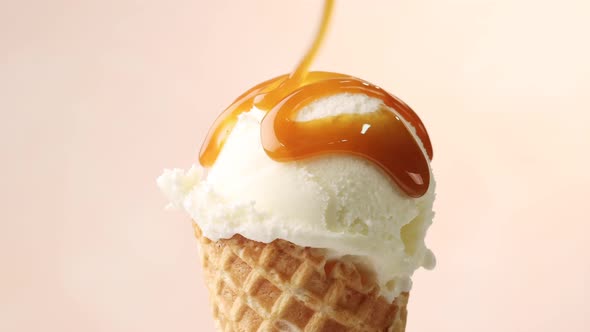 melted caramel sauce flowing on vanilla ice cream scoop in waffle cone close up on beige background