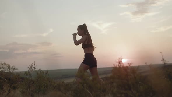 Female boxer in black sport suit warms up at sunset before starting a training session in the field.