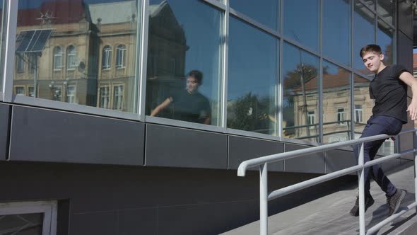 Shot of Casual Guy with Well Clothes Sitting on a Railing in the Street