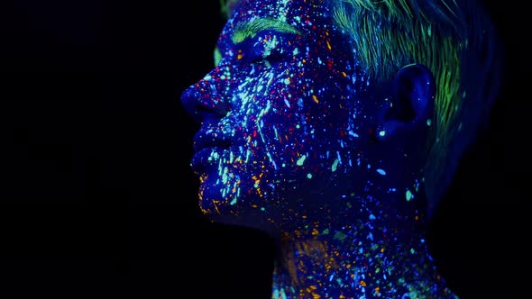 Man Face Painted with Fluorescent Colors in Profile Turns Head and Looks Into Camera