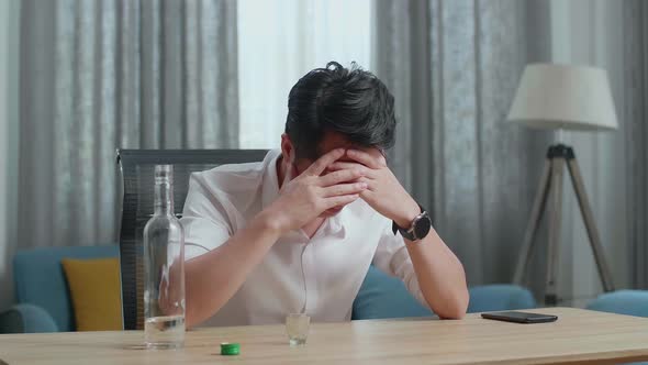 Drunk, Depressed Asian Man With Smartphone On Table Pouring Vodka In A Shot Glass Before Drinking