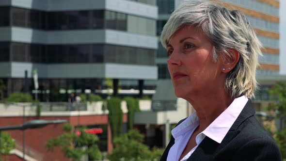 Business Middle Age Woman Looks Around - Company Buildings in the Background - Closeup of Face