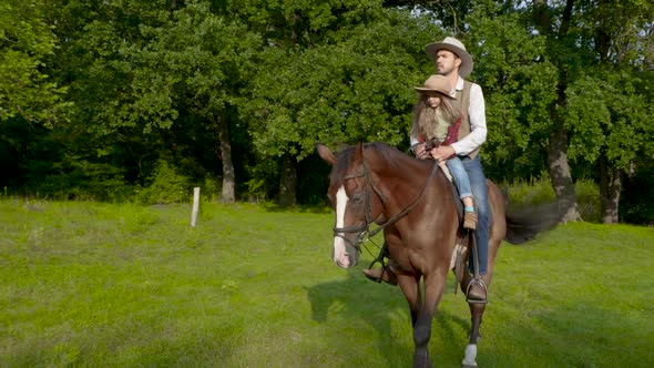 Cowboy and His Daughter on Horseback on a Forest Lawn