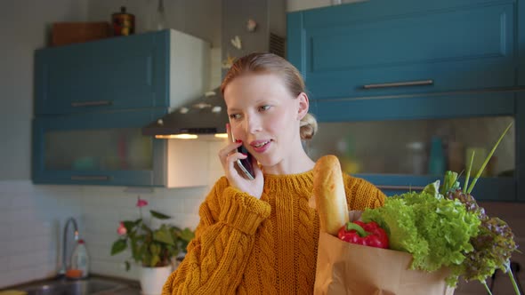 Beautiful Young 30s Woman on Kitchen with Package Fresh Products in Hands Call Phone