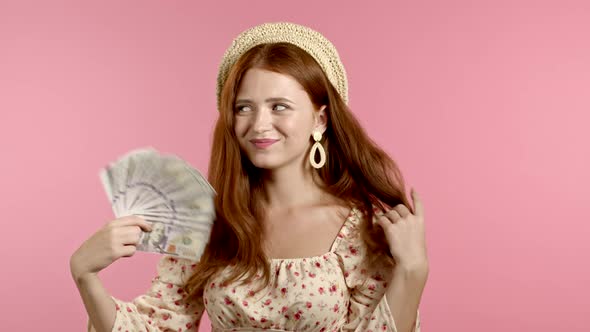 Amazed Happy Excited Woman Showing Money - U.S. Currency Dollars Banknotes on Pink Wall. Symbol of