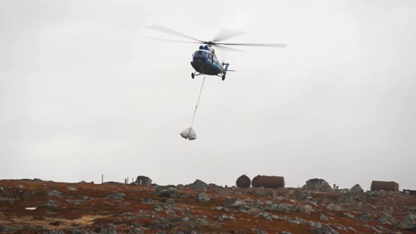 Mi-8 Helicopter Lands with Cargo-white Bags Swinging Under It, Hanging on Ropes
