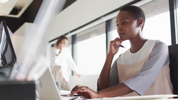 Two diverse female colleagues working at desk with laptop and smartphone