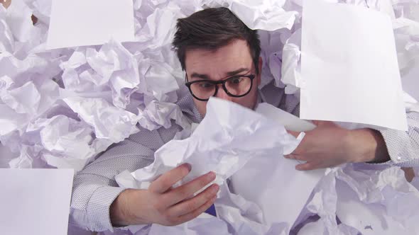 Perplexed Man Office Worker in Glasses in a Large Heaps of Crumpled Paper