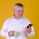 Handsome adult man with a mug of coffee or tea uses smartphone texting messages - VideoHive Item for Sale