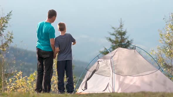 Young father with his child son resting together near a hiker tent in summer mountains. Active