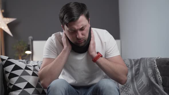 Disabled Man with Neck Brace Talking on Phone with Doctor Experiencing Pain While Sitting on Couch