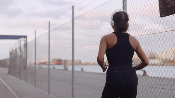 Young Woman In Sportswear And Headphones Jogging Along Harbour