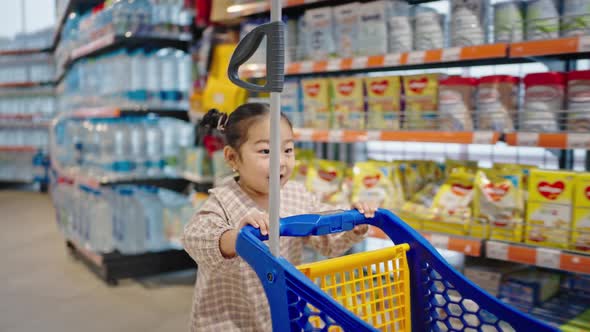 Excited Asian Girl Runs with Blue Cart About Supermarket