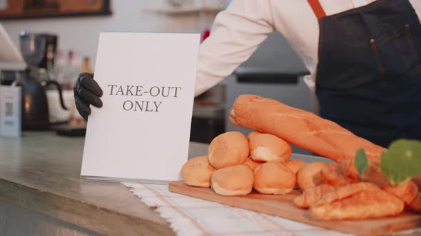 Close up of cafe business owner or barista put TAKE OUT ONLY sign on coffee bar counter