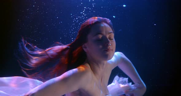 Close-up of a Dark-haired Young Girl, She Is in a Studio Under Water on a Blue Background, She Is