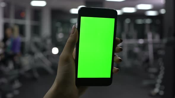 Female Hand Holding Smartphone in Gym, Green Screen, Online Fitness Application