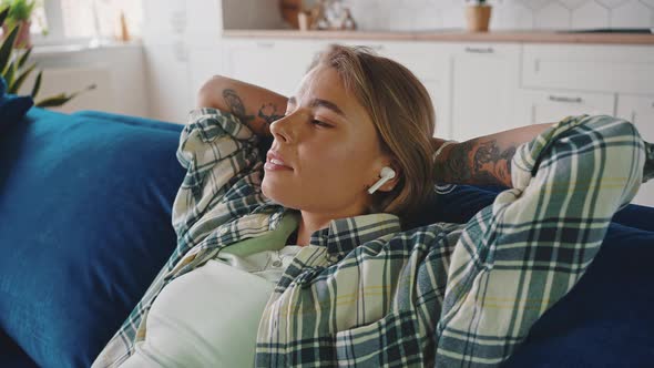 Close Up Portrait of Young Blonde Woman Listening to Audiobook in Wireless Headphones Resting on