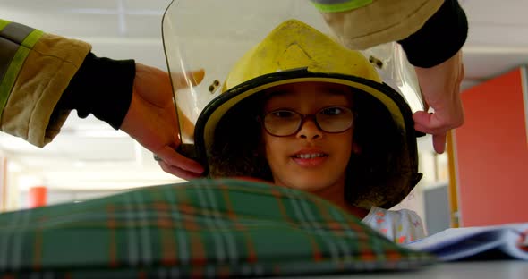 Firefighter helping African American schoolgirl by putting helmet on her head in classroom at school