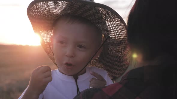 Happy Little Toddler Boy in Hat Having Fun Sitting in Parents Arms in Field in Summer at Sunset