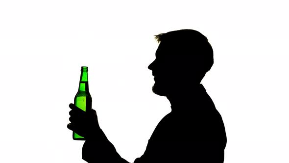Man in the Room Sits Opens and Drinks From the Bottle. Side View. Silhouette White Background