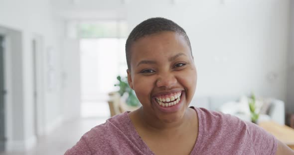 Portrait of smiling african american plus size woman looking at camera and laughing in living room