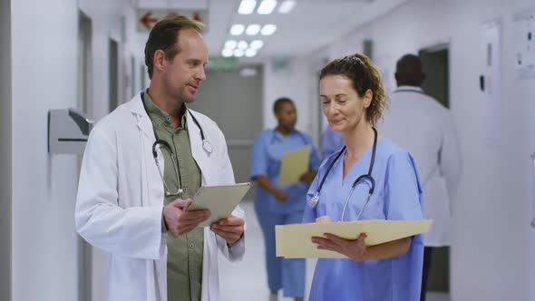 Caucasian male and female doctor talking in hospital corridor looking at tablet and patient files