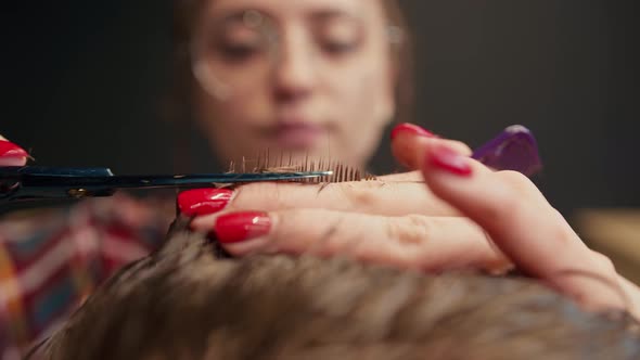 Barbershop, close-up: woman barber cuts men's hair with scissors