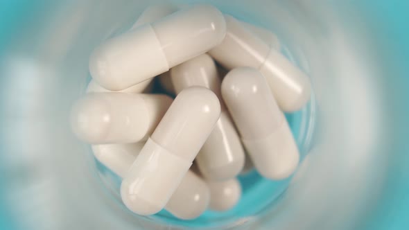 White medicinal capsules close-up. In a glass pharmaceutical bottle in blur 