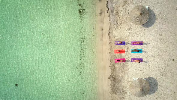 Aerial view of group of people in yoga pose on colourful mats on the beach.