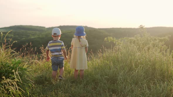 Cute Preschool Little Baby Girl and Boy Sitting on Top of Mountain in Tall Grass Before Sunset