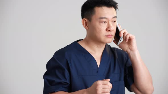 Serious Asian doctor talking with patient by phone