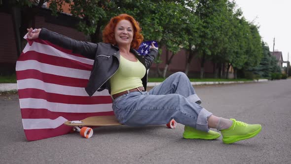 Happy Retro Woman Sitting on Skateboard with USA Flag Looking at Camera Smiling