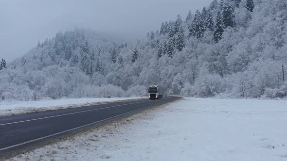 Aerial shot: cars and trucks are driving by the road in winter forest.