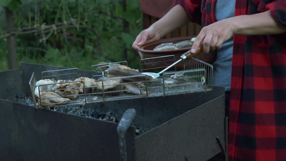 Close up of woman hands put cooked grilled fish on plate. Family on bbq picnic at summer cottage