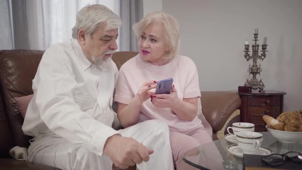 Modern Senior Caucasian Woman Teaching Her Elegant Husband To Use Smartphone, Intelligent Mature