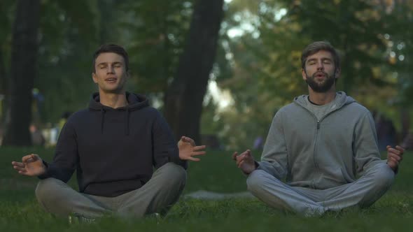 Male Friends Sitting in Lotus Position, Practicing Yoga in City Park, Meditation