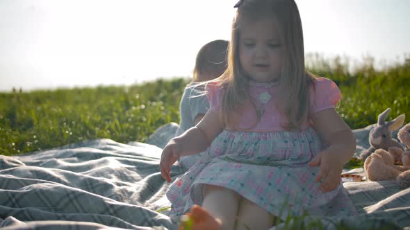 Two Small Sisters Are Sitting on a Picnic Cover.