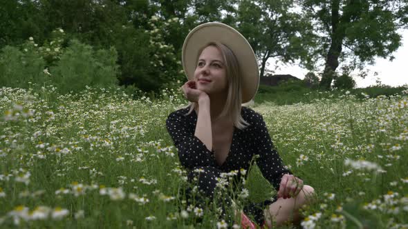 Blonde girl in dark dress in a chamomiles flowers meadow