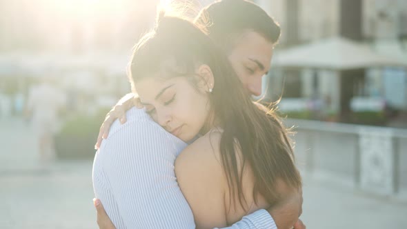 Hispanic Couple Embracing on Embankment in Sunny Town